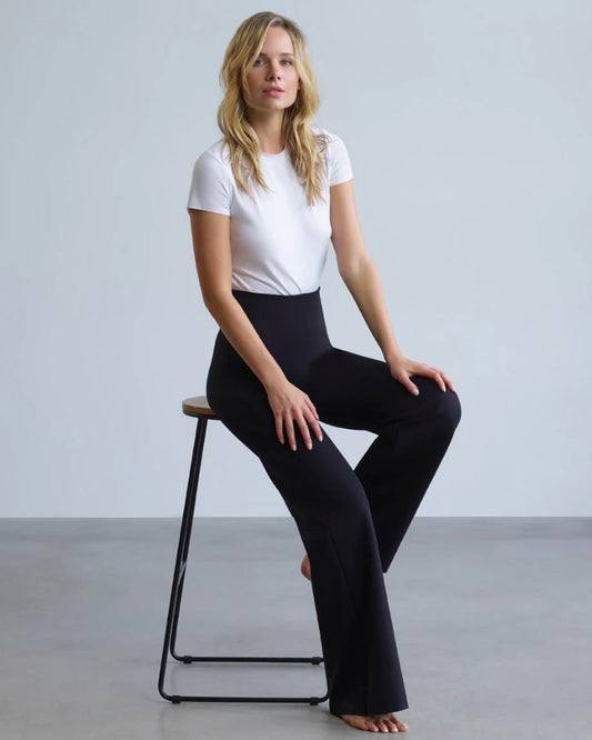 Model wearing Commando Neoprene Wide Leg Pants wearing white tee sitting down on a chair on a white background