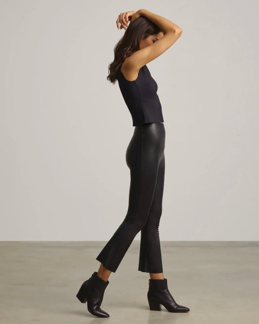 Model standing sideways wearing Commando Faux Black Leather Cropped Flare pants with black tank top and black boots on a white background