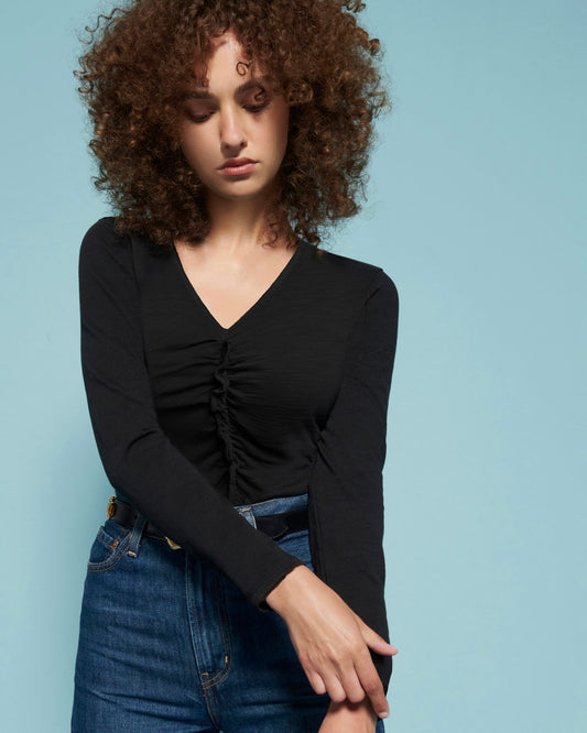 Model wearing Nation Cambria Gathered Long sleeve shirt in black wearing jeans on a blue background