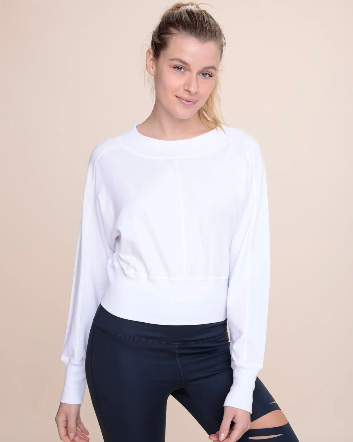 Model wearing Mono B Dolman Sleeve Paneled Top in white wearing black pants with hole in knee on a beige background