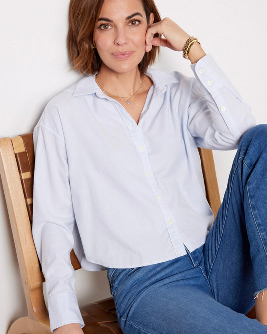 Model wearing Faherty Stretch Oxford Cropped Shirt wearing jeans sitting in a chair