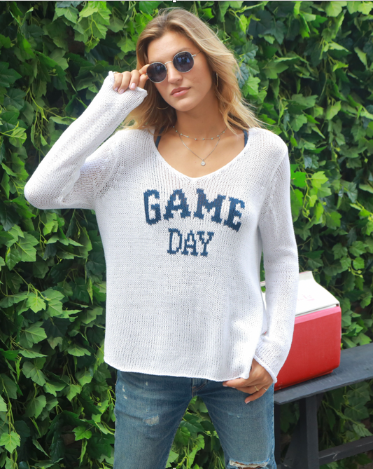 Model wearing Wooden Shops Game Day Sweater wearing jeans and sunglasses standing in front of leaves