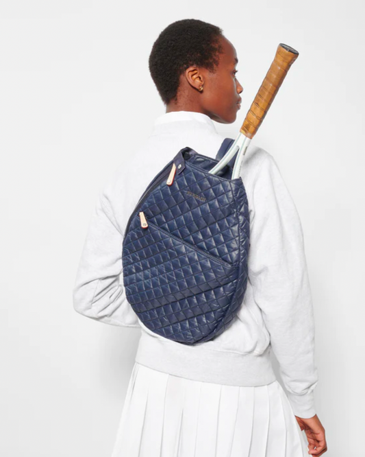 Model wearing a Mz Wallace Metro Racquet Sling tennis bag over the shoulder in Dawn Blue color wearing a white sweatshirt and white tennis skirt on a white background