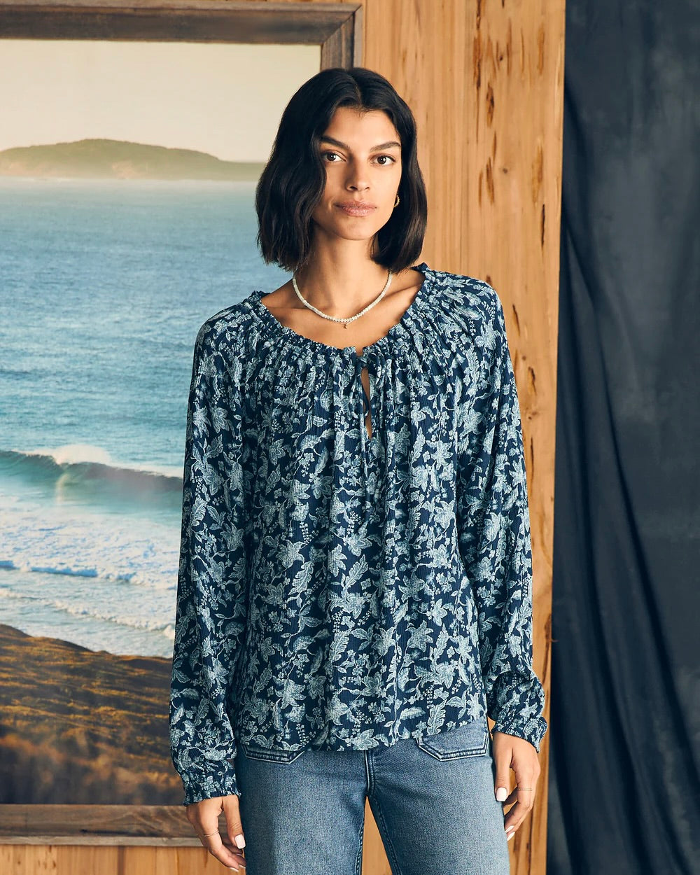 Model Wearing Faherty Emery Blouse wearing jeans standing in front of ocean painting