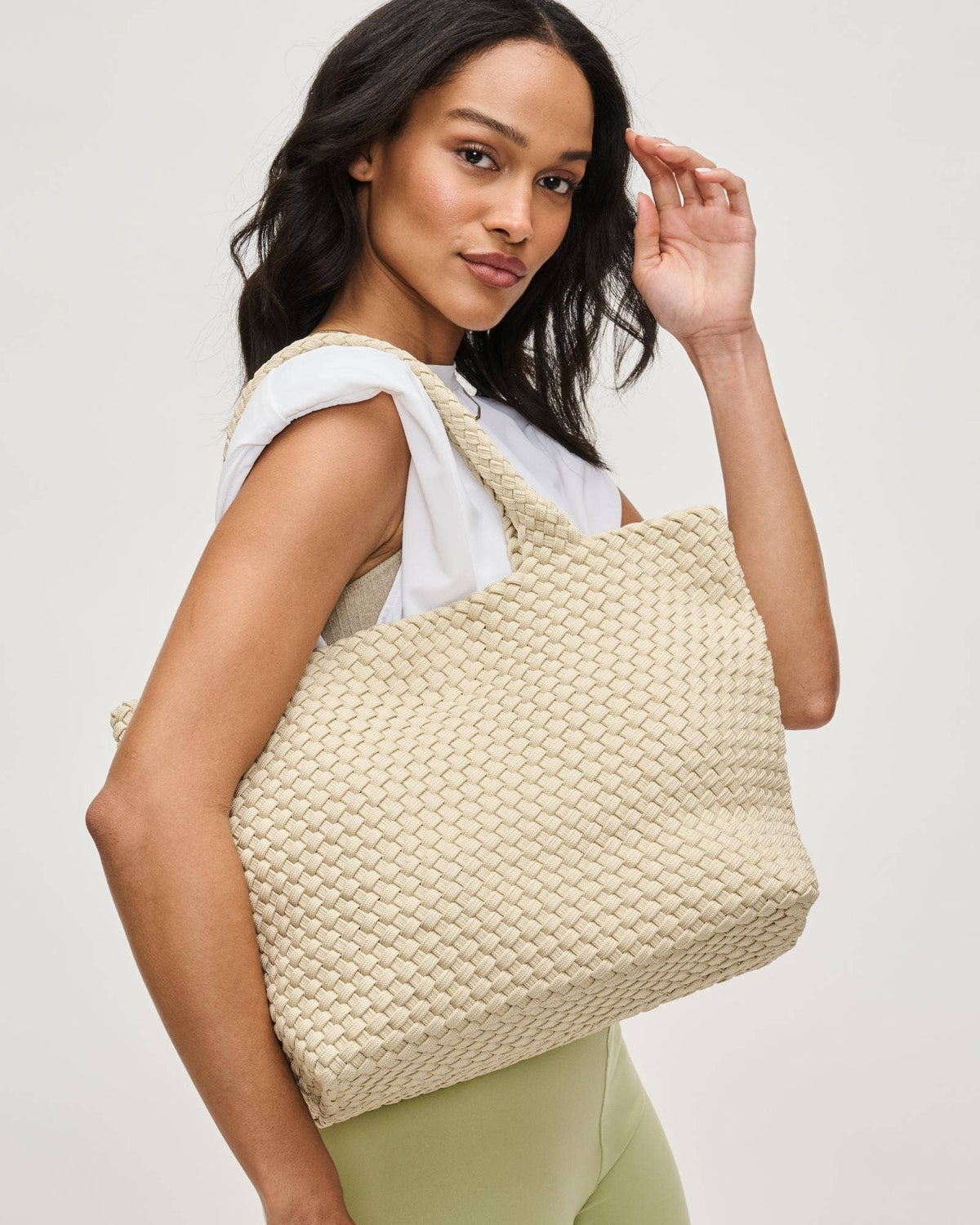 Woman holding a woven beige handbag against a plain background