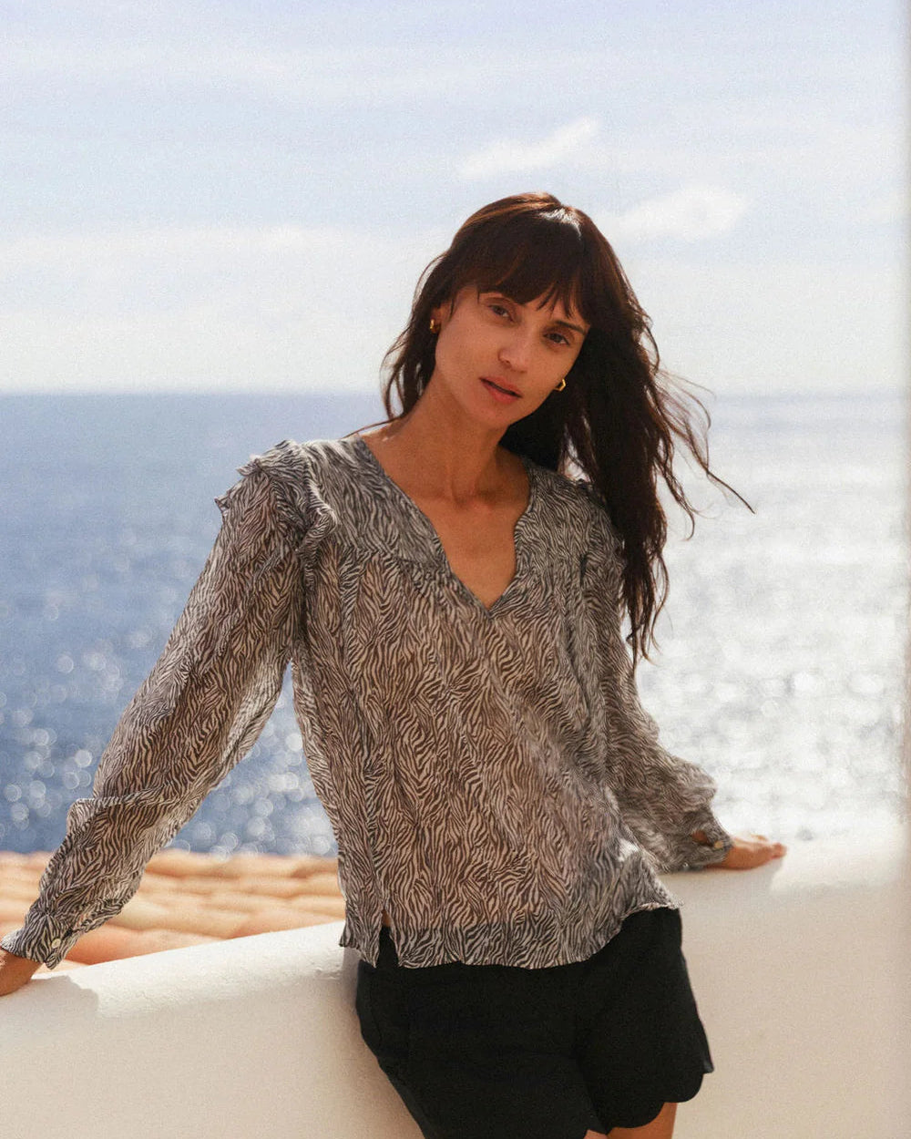 Woman standing by a window with a scenic view of the ocean.