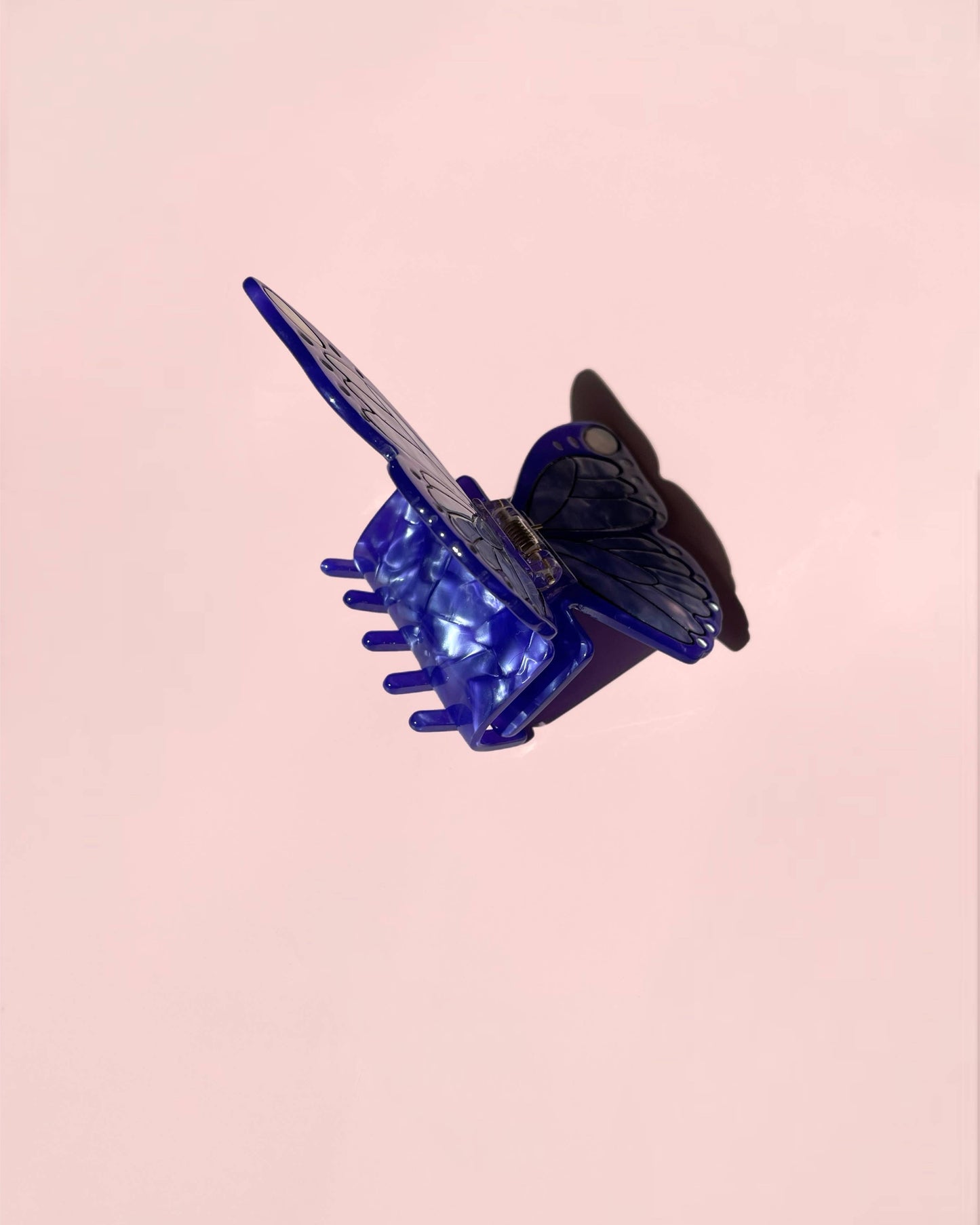 Blue hair clip with a black butterfly design on a pink background