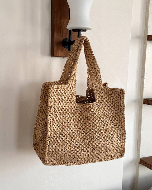 Woven brown bag hanging on a white wall with wooden shelves in the background
