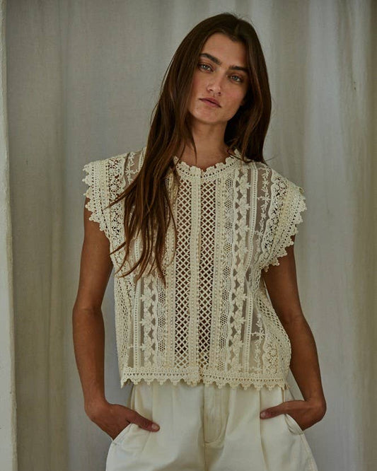 Woman wearing an off-white lace top and shorts against a neutral background
