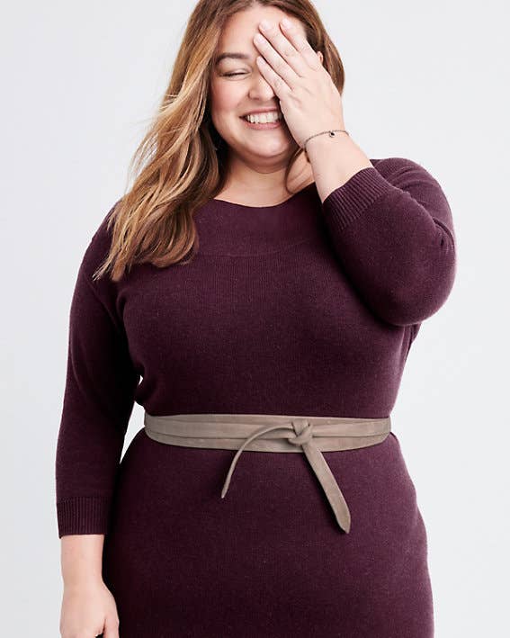 Woman wearing a burgundy sweater dress with a beige belt on a white background