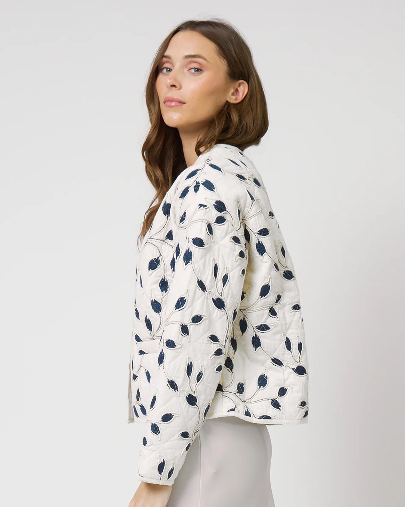 Woman wearing a white jacket with blue floral patterns on a plain background