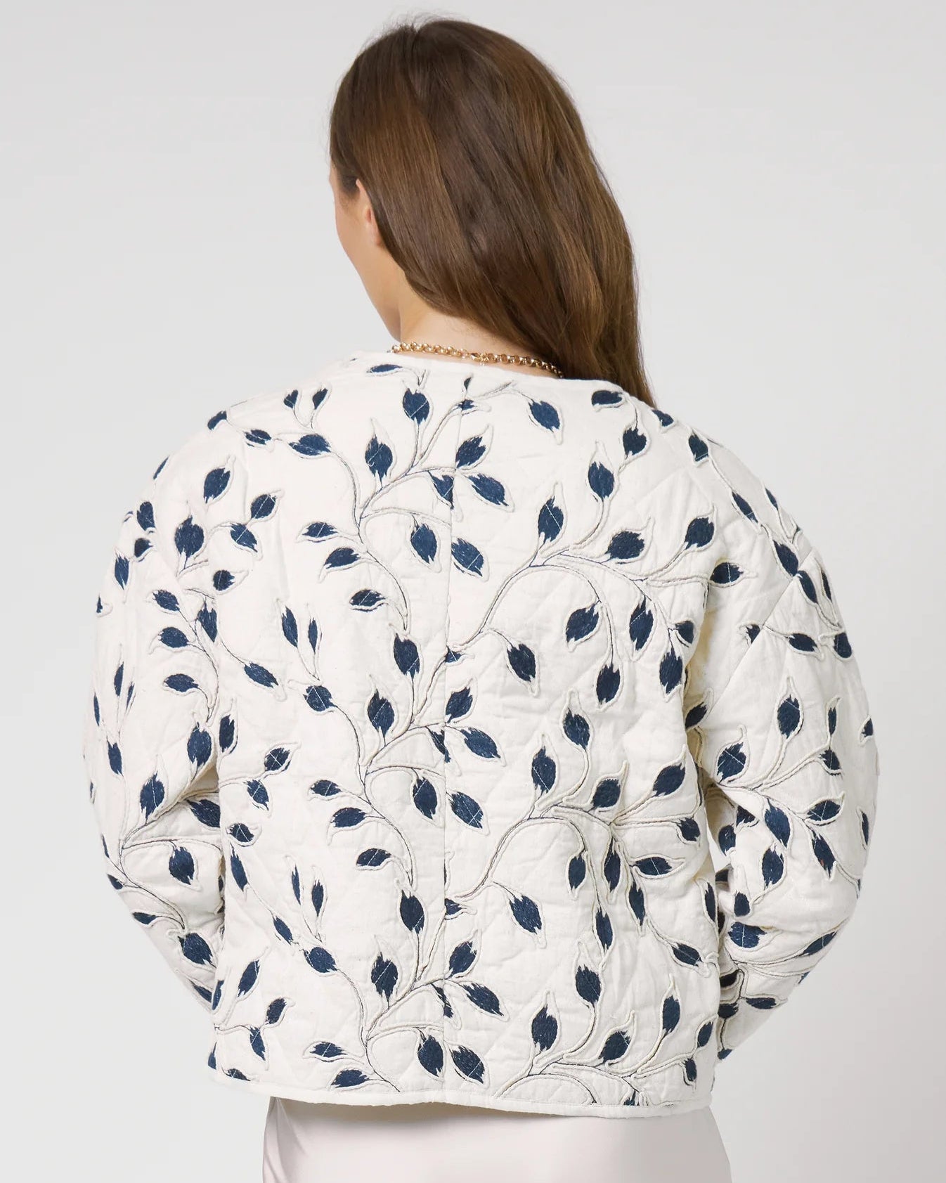 Woman wearing a white floral patterned jacket on a plain background