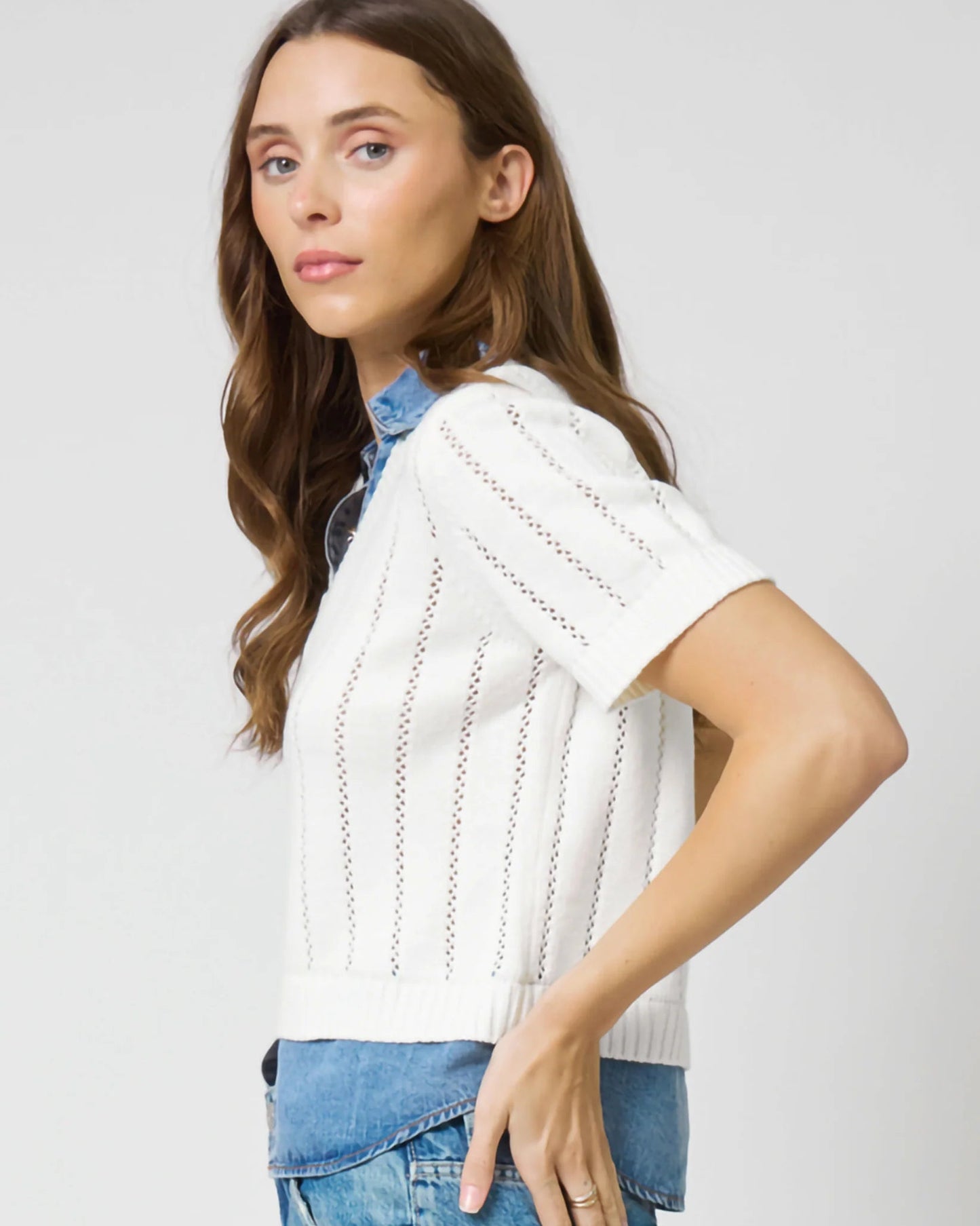 Woman wearing a white knitted top and blue jeans against a plain background