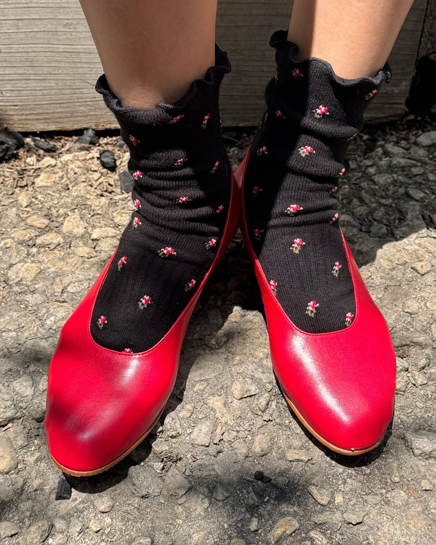 Red shoes with black socks featuring pink patterns on a textured ground.