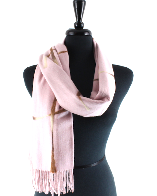 A light pink scarf with a subtle gold geometric pattern and fringed ends, draped on a black mannequin torso against a white background.
