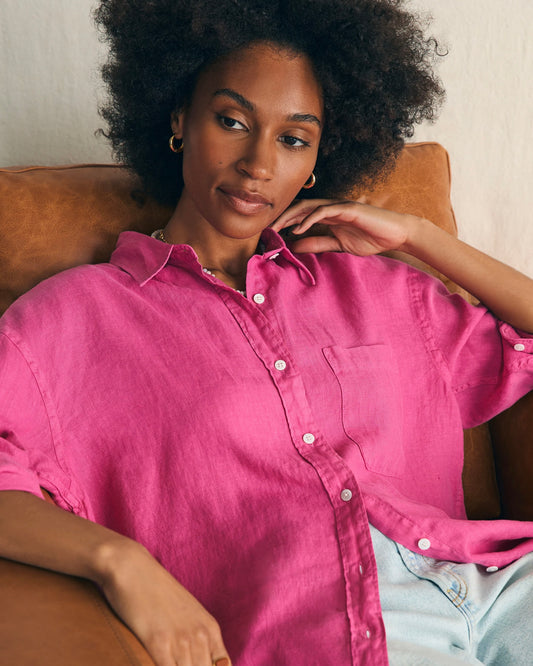 Model wearing Faherty Laguna Linen Relaxed Shirt in cone flower pink sitting in a brown leather chair