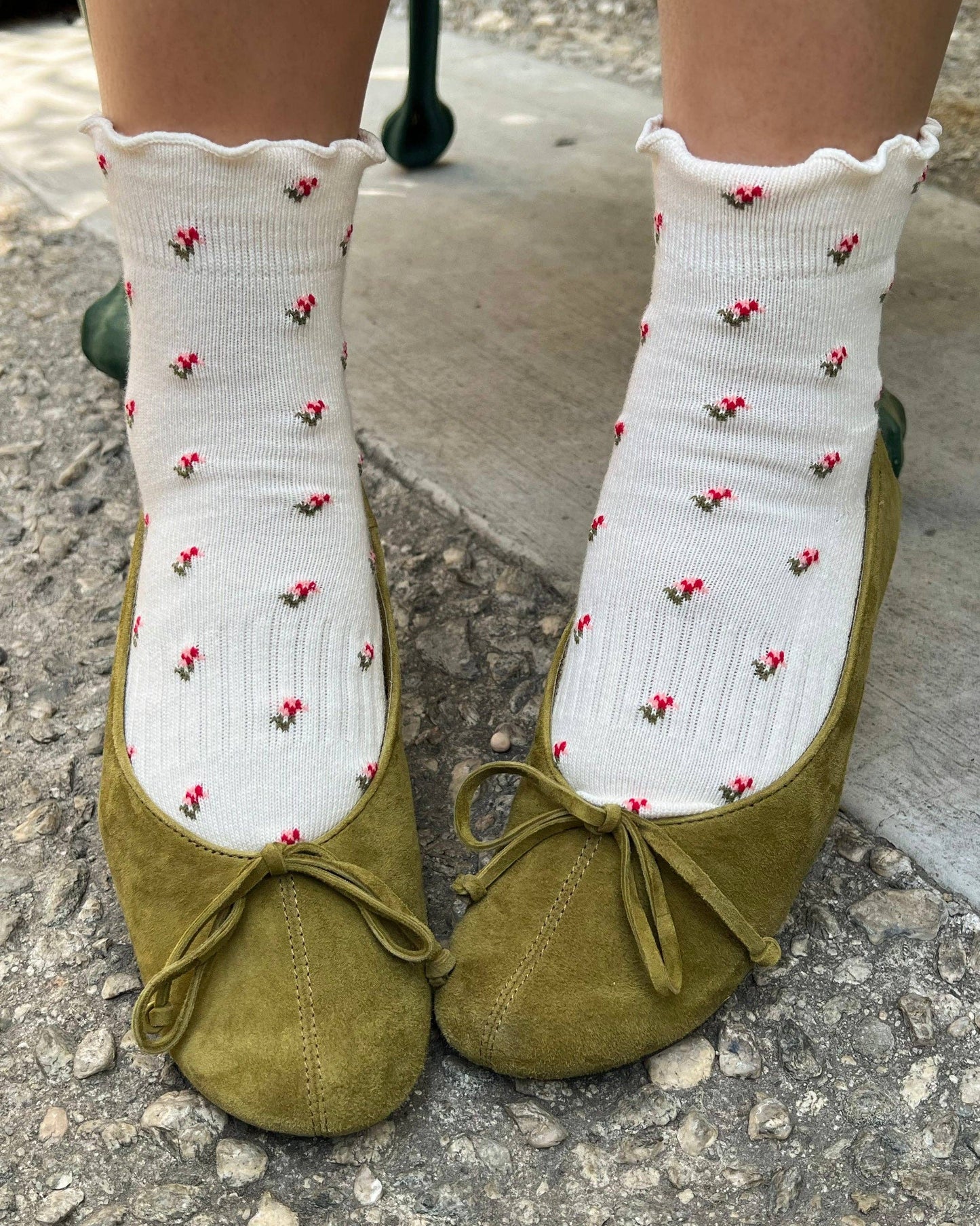 Green shoes with white socks featuring red patterns on a stone surface