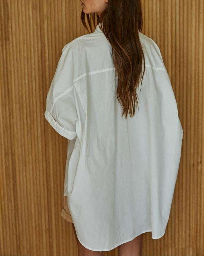Woman wearing a white oversized shirt against a wooden paneled wall