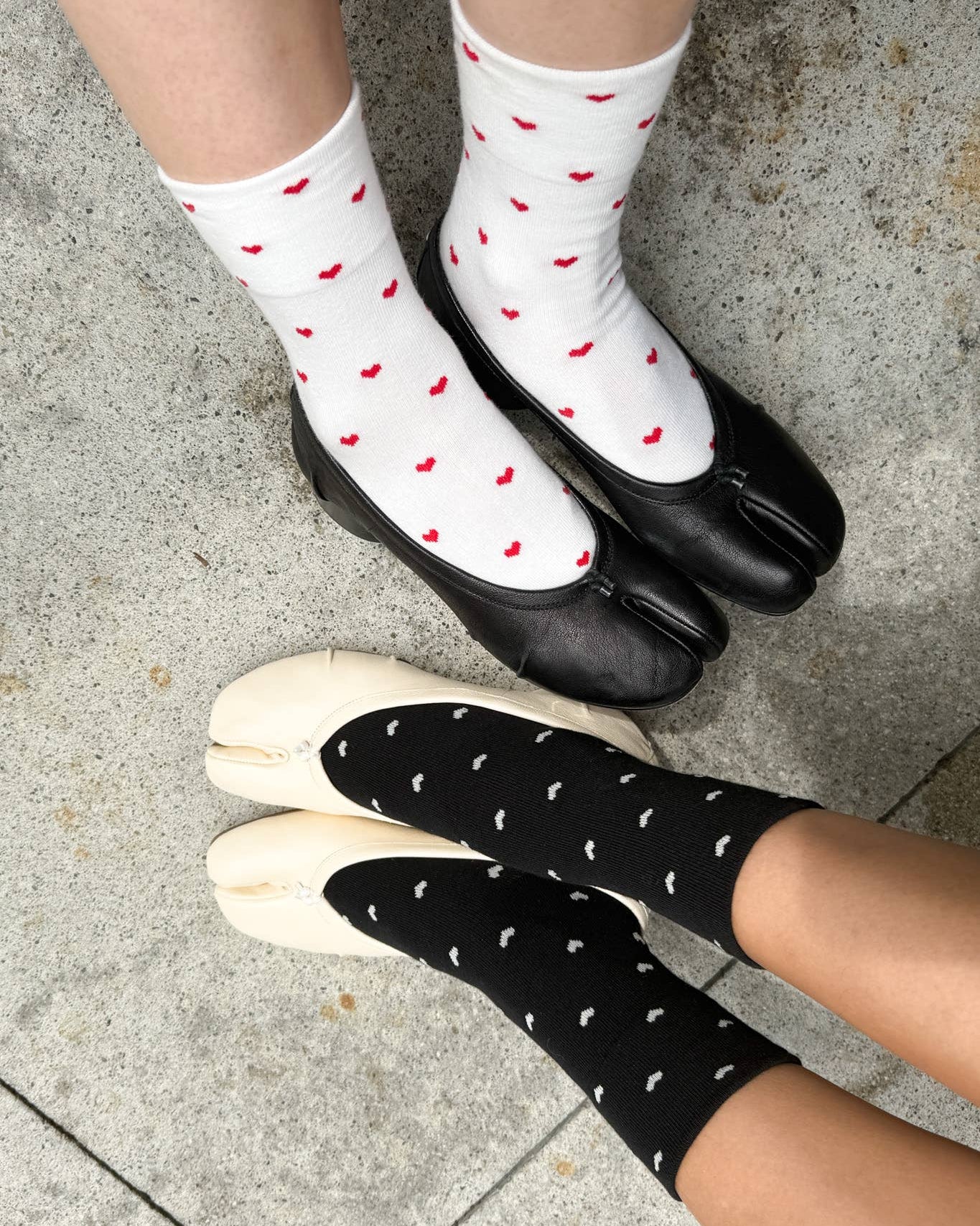 White socks with red hearts and black socks with white dots worn by two people on a concrete floor.