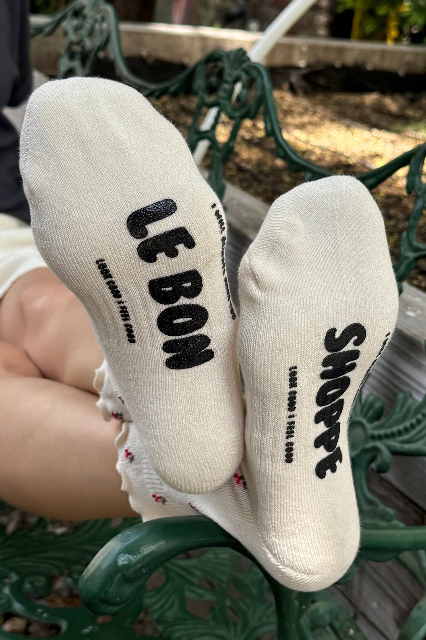 White socks with black text worn by a person sitting on a green metal bench.