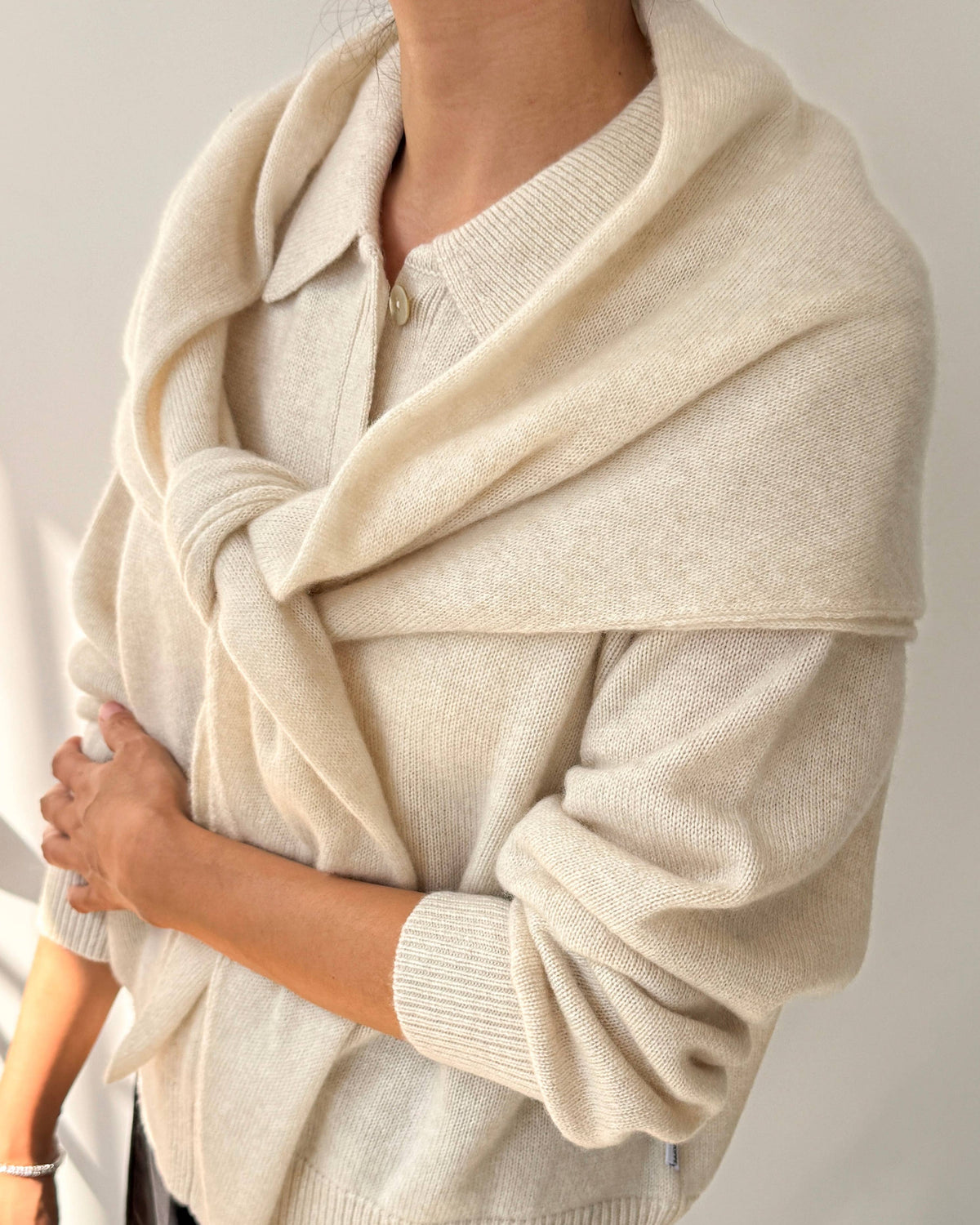 A person wearing a cream-colored knit cardigan with a large draped shawl collar, styled over a white top and black pants.