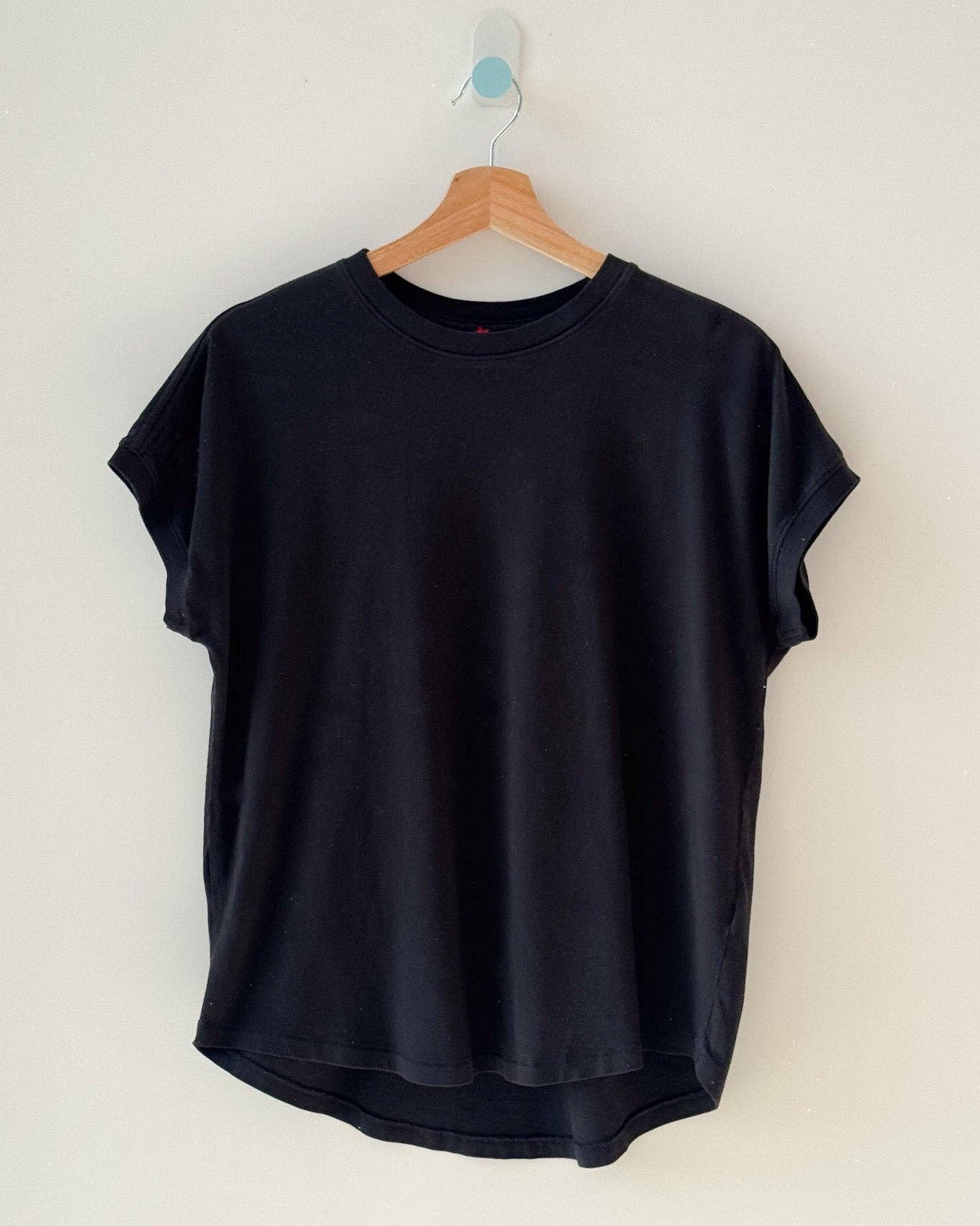 Black t-shirt on a wooden hanger against a white wall