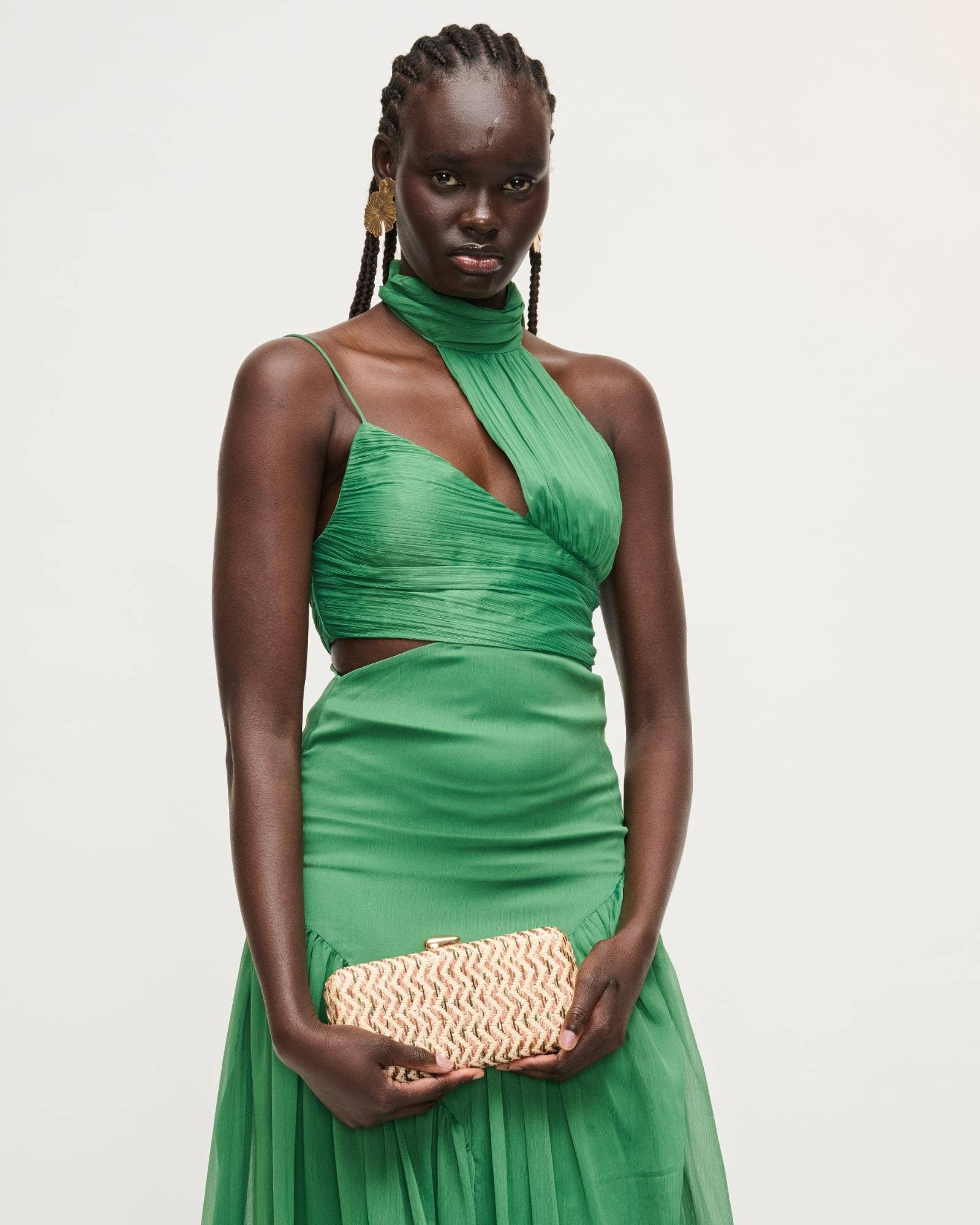 Woman wearing a green dress holding a beige clutch against a white background