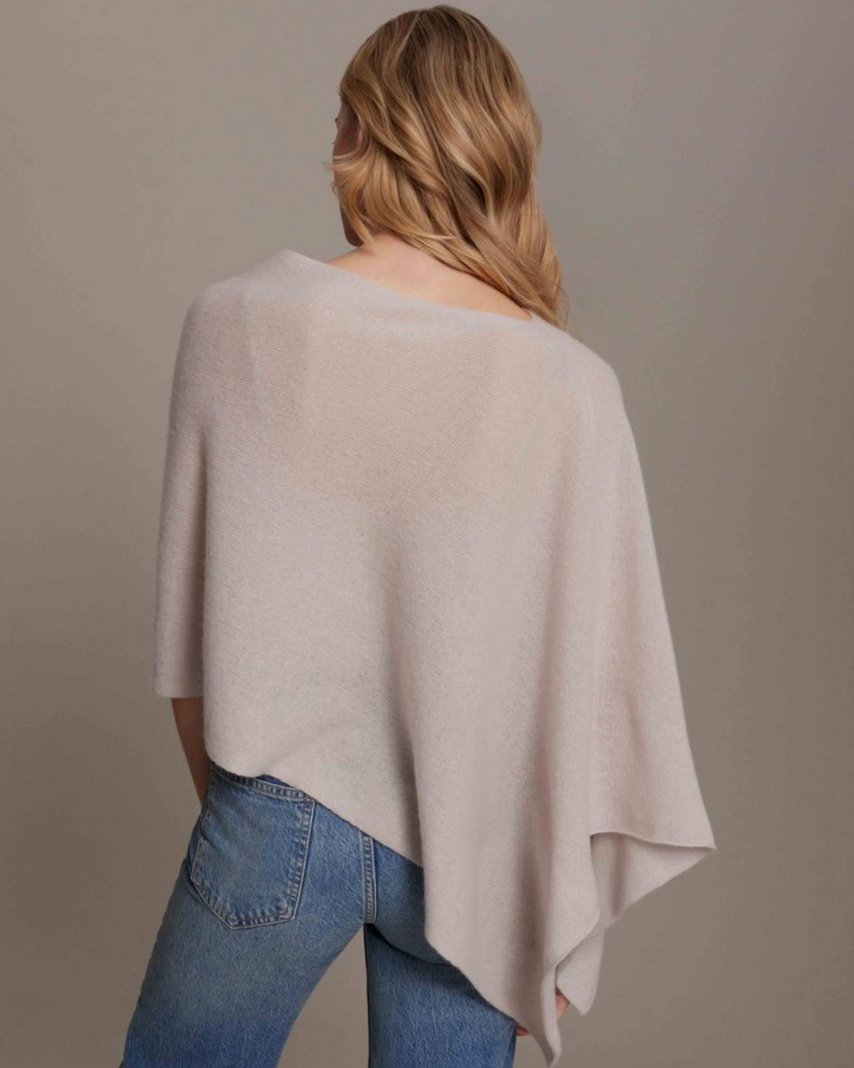 Woman wearing a beige poncho over a plain background