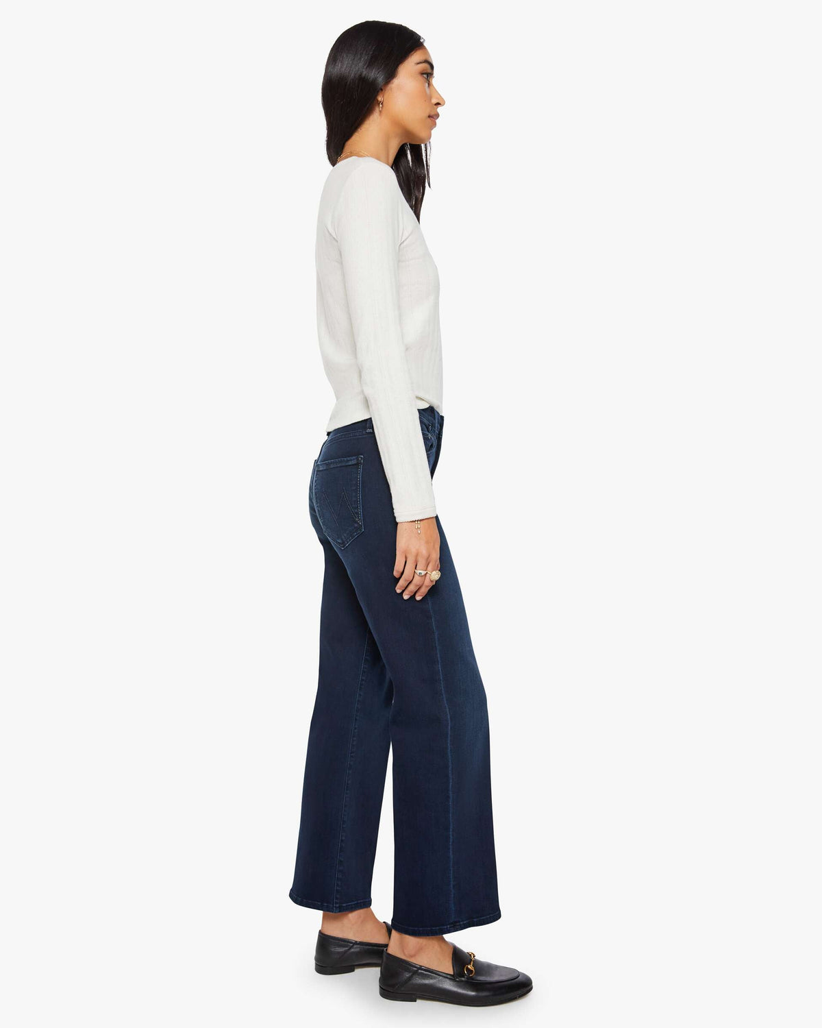 Woman wearing a white long-sleeve top and dark blue wide-leg pants on a white background