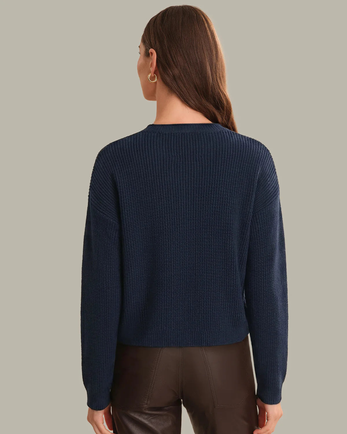Person wearing a navy blue sweater and brown pants on a plain background