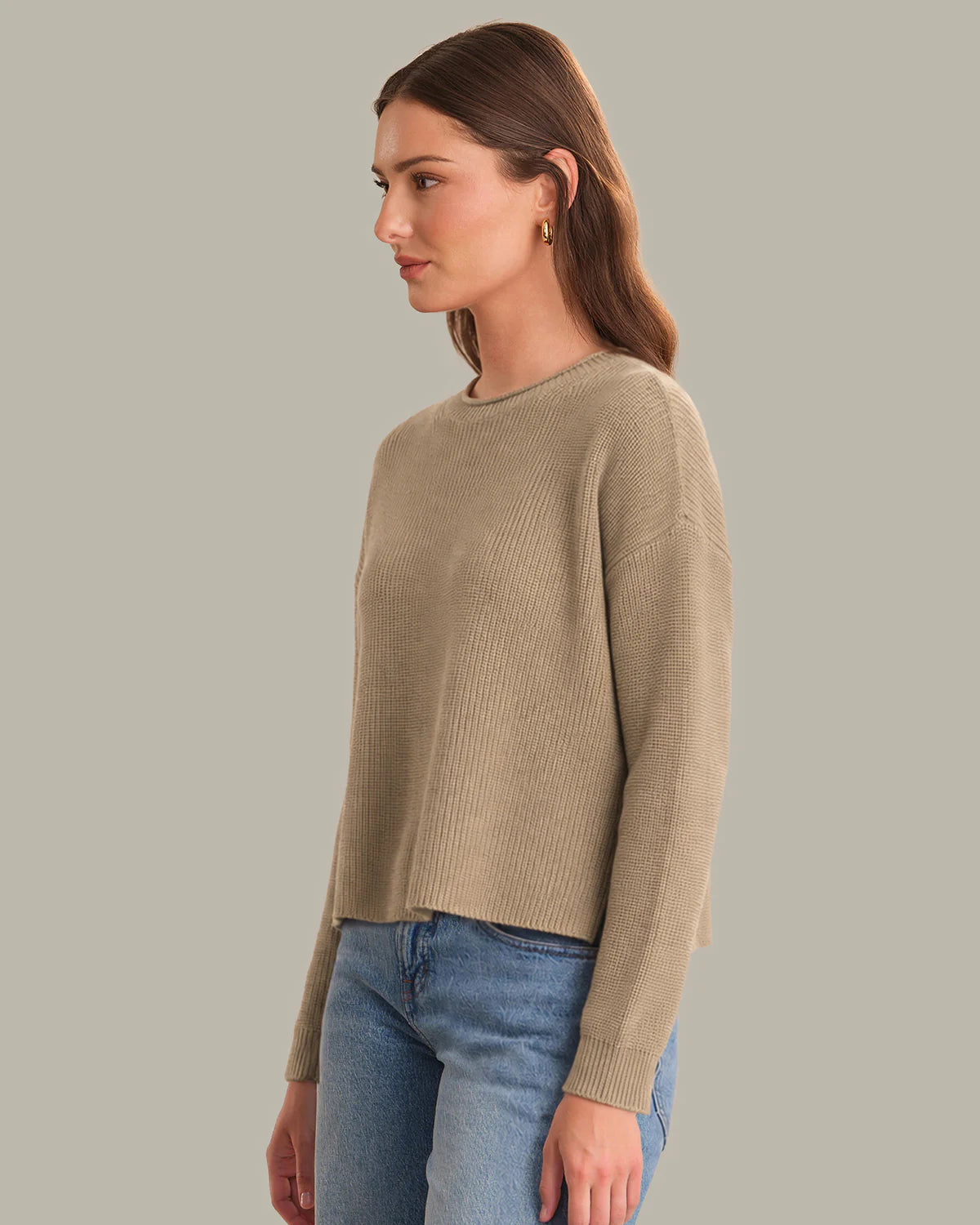 Woman wearing a beige sweater and blue jeans against a gray background