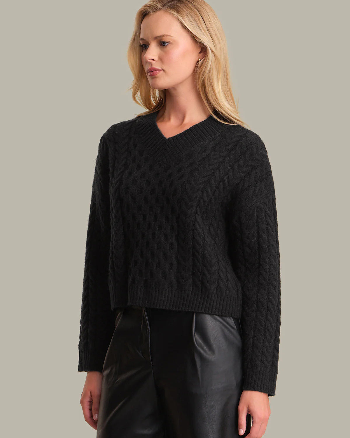 Woman wearing a black cable knit sweater against a neutral background