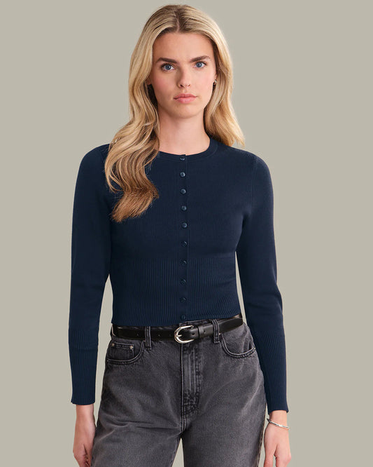 Woman wearing a navy button-up shirt and gray jeans against a plain background