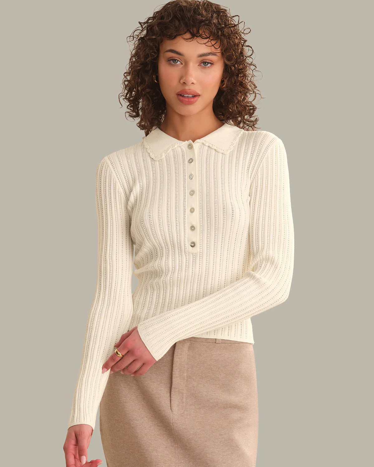 Woman wearing a cream ribbed sweater over a beige shirt with a plain background