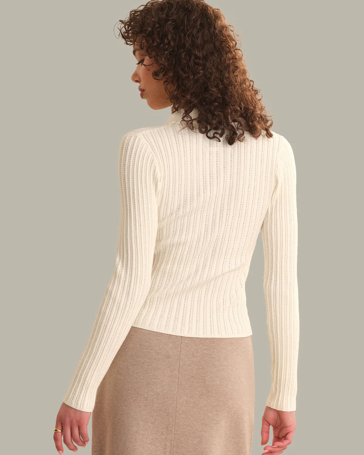 Woman wearing a cream ribbed sweater against a gray background