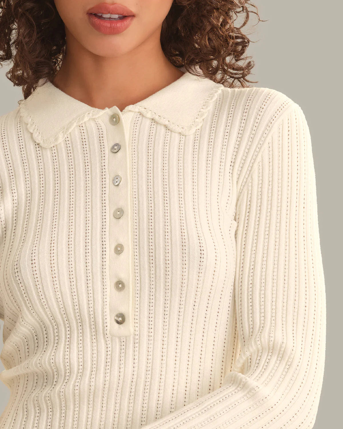 A close-up of a woman wearing a cream-colored ribbed knit long-sleeve top with a buttoned henley-style collar.