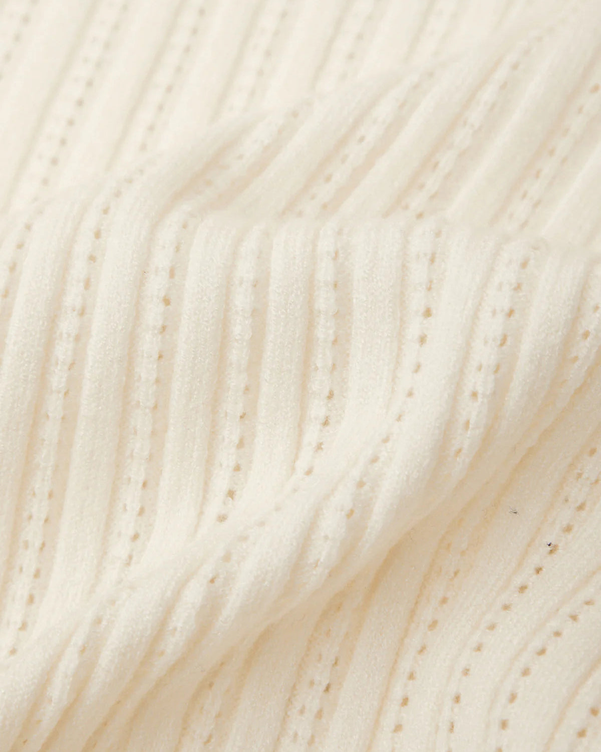 Close-up of a cream-colored ribbed knit fabric with vertical channels and small dotted stitch details.