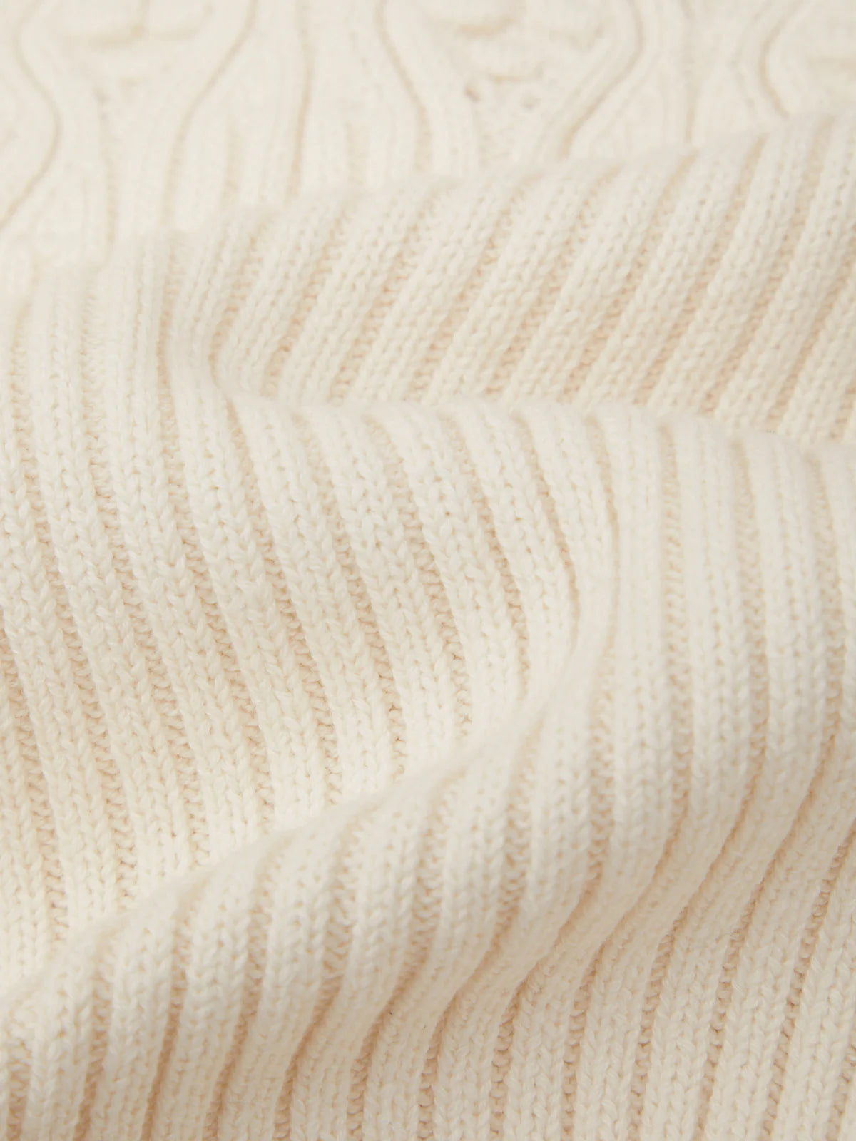 Close-up of a cream-colored ribbed knit fabric with a textured cable pattern visible in the upper section.