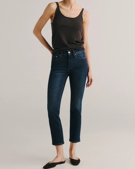 A model wearing dark blue cropped jeans, a black tank top, and black flat shoes, standing against a light gray studio background.
