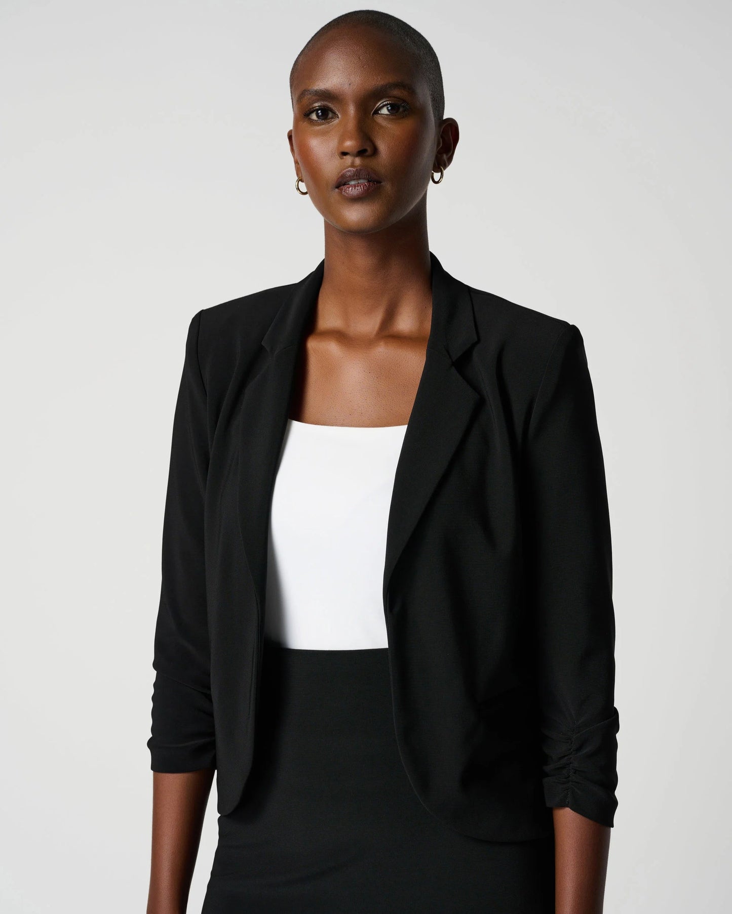 Woman wearing a black blazer over a white top and black skirt on a white background