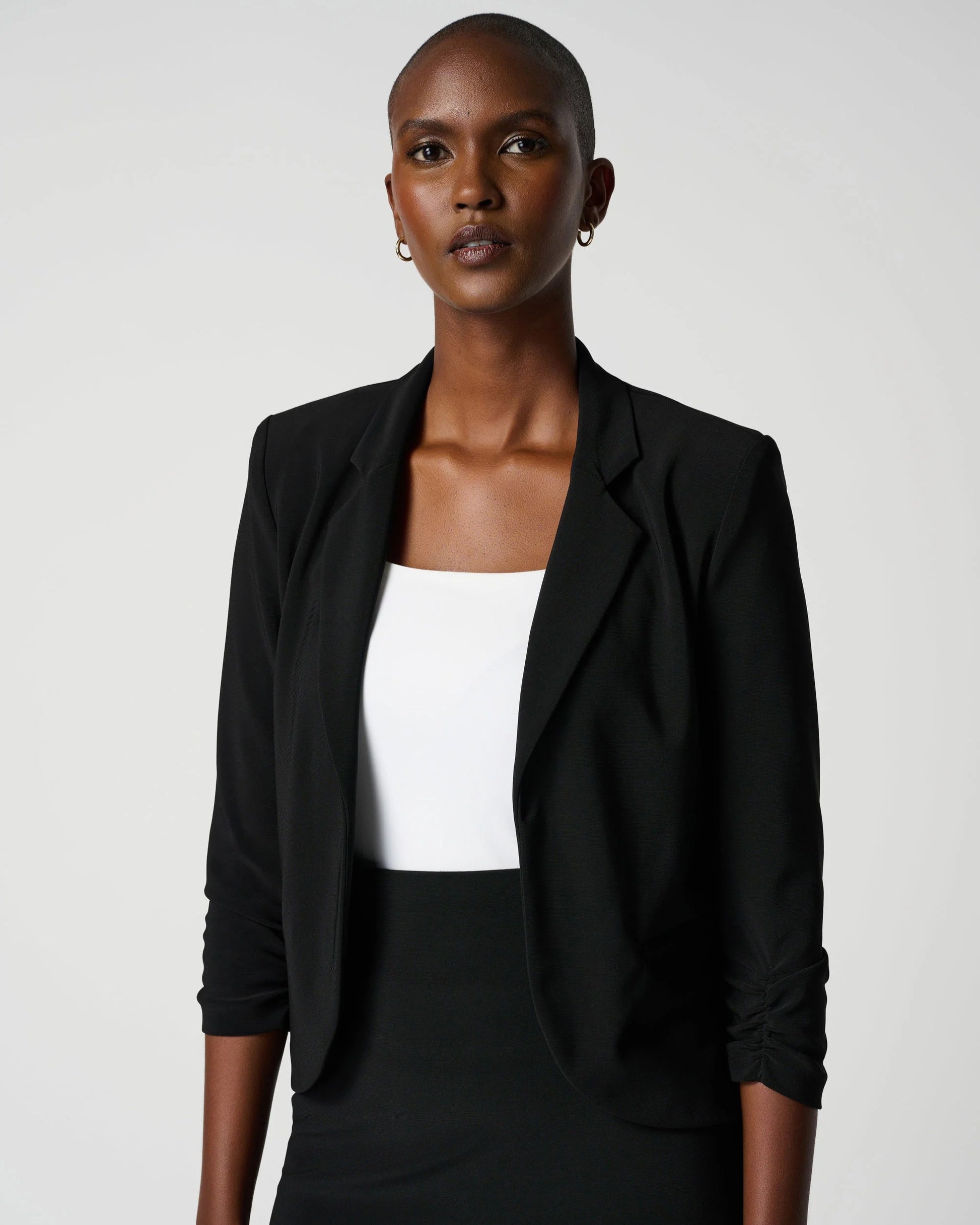 Woman wearing a black blazer over a white top and black skirt on a white background