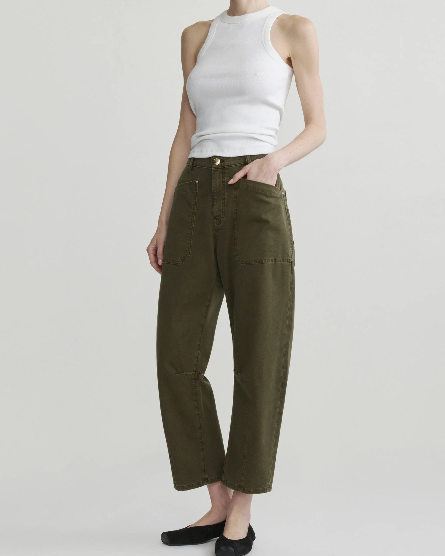 A model wearing olive green cropped wide-leg pants with a white ribbed tank top and black flats, standing against a light gray studio background.