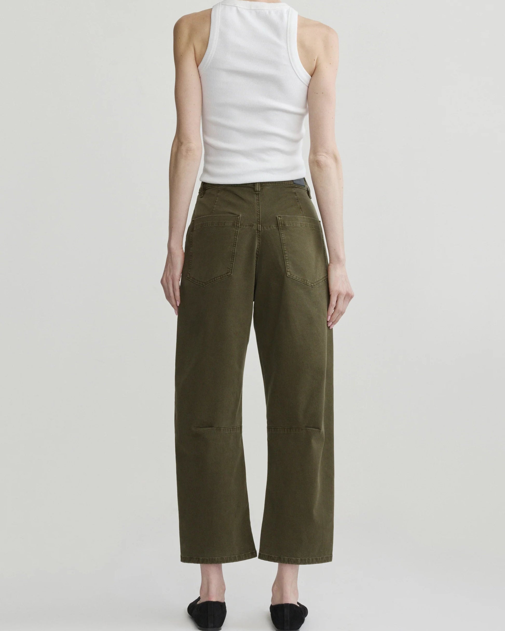 A model shown from the back wearing olive green wide-leg cropped pants, a white ribbed tank top, and black flats against a light gray studio background.