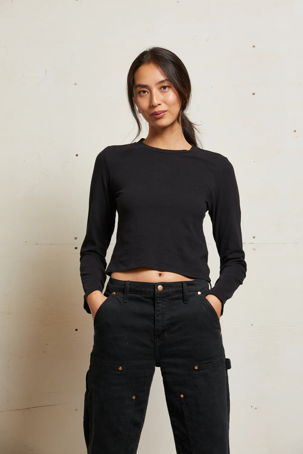 Woman wearing a black long-sleeve top and black pants against a neutral background