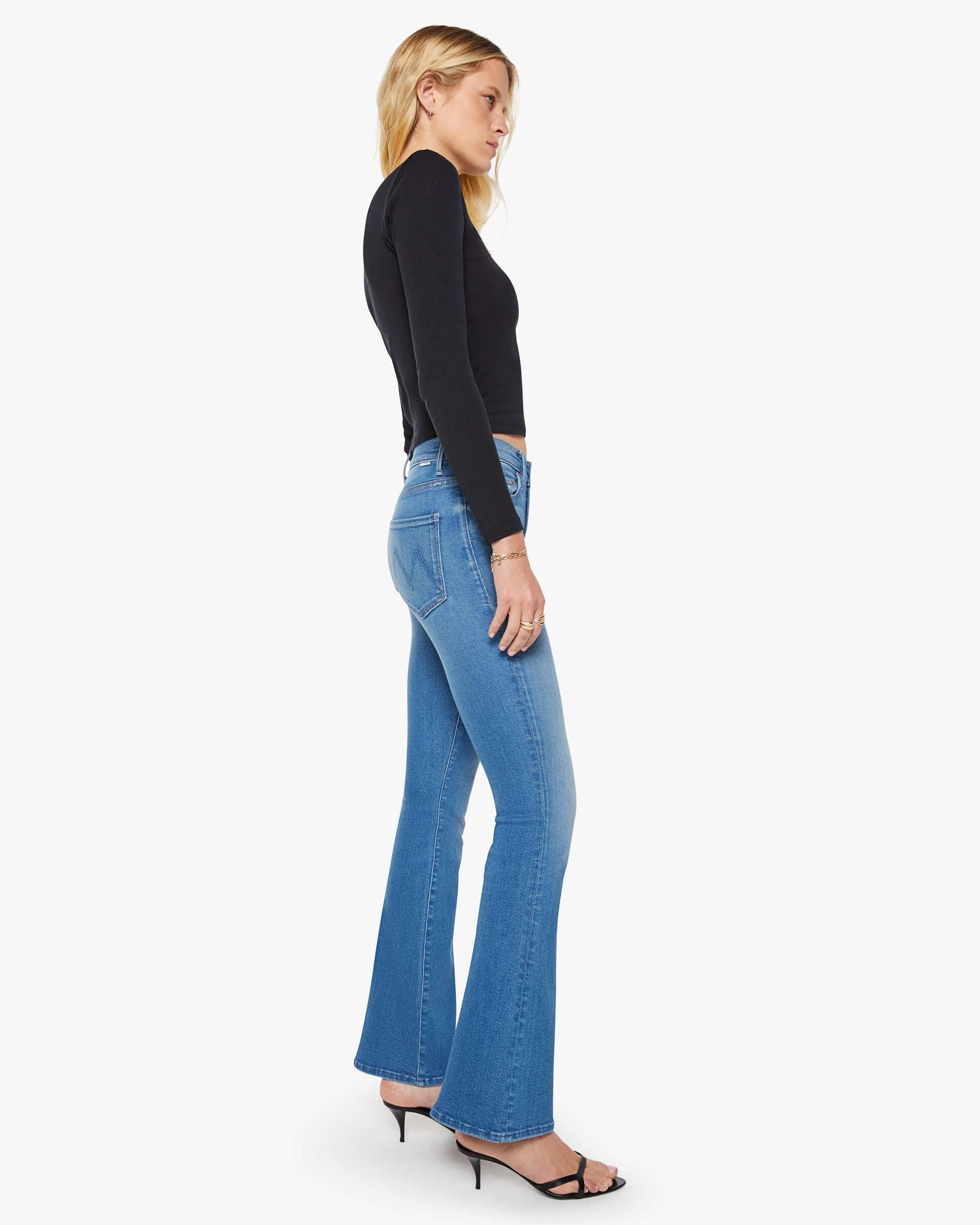 Woman wearing blue flared jeans and a black top on a white background