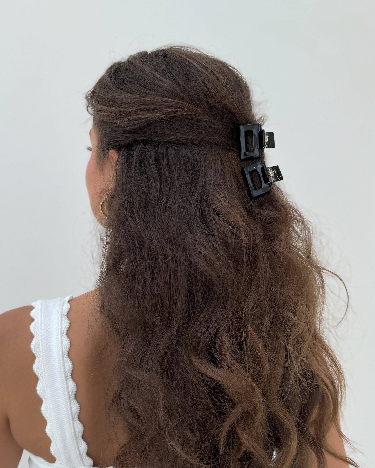 Person with wavy hair wearing a black hair clip on a white background