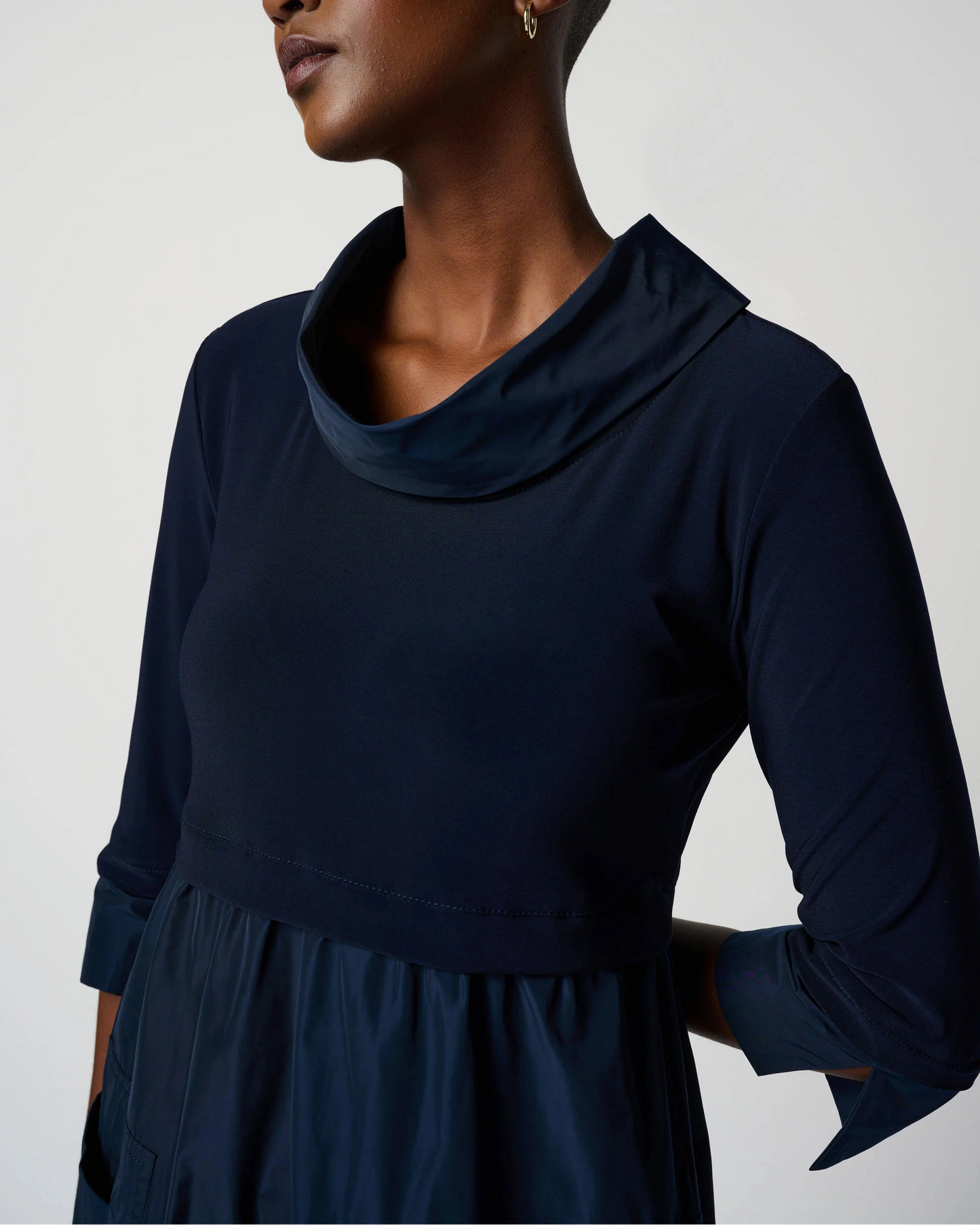 Woman wearing a navy blue dress with a cowl neckline on a white background