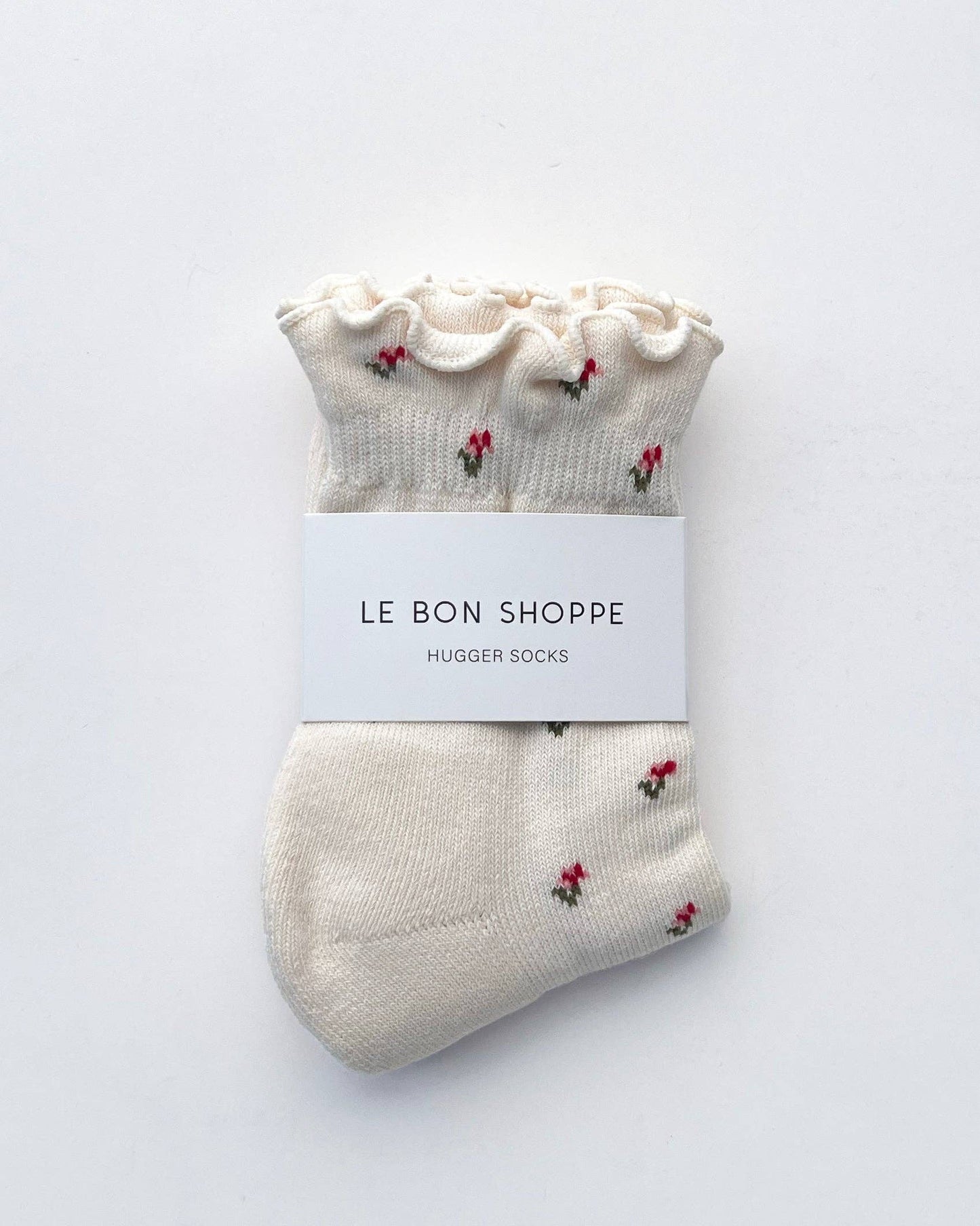 Pair of white socks with red floral patterns on a white background, labeled 'Le Bon Shoppe'.