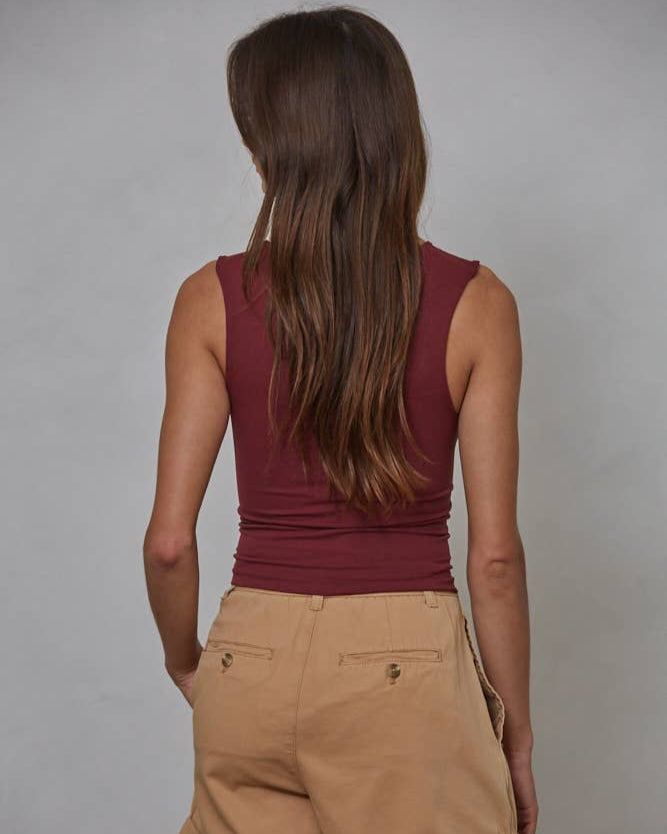 Back view of a woman wearing a maroon tank top with beige shorts against a gray background.
