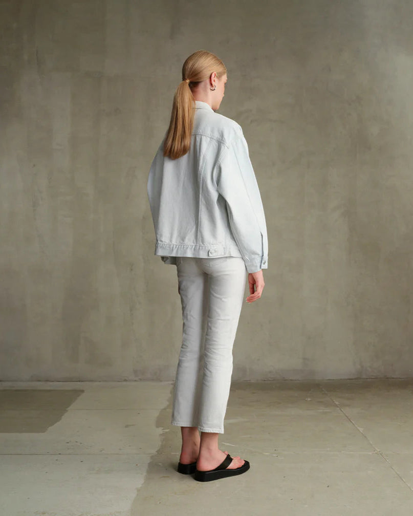 Person wearing a light gray jacket and pants standing against a plain wall.
